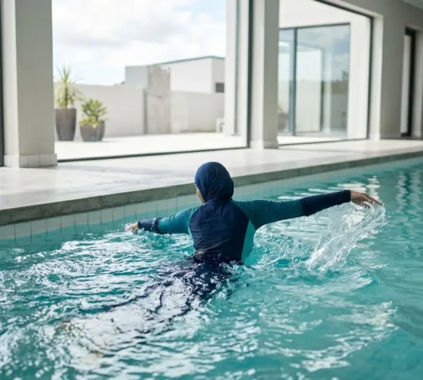 Une femme en burkini moderne vue de dos effectue un mouvement de brasse dans une piscine lumineuse aux lignes contemporaines